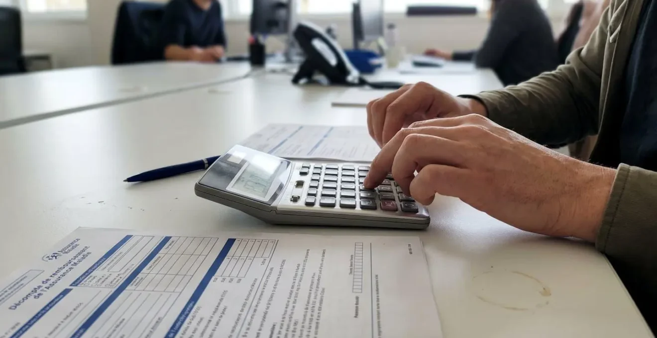 Jeune couple assis à une table de cuisine lumineuse, consultant ensemble des documents administratifs de santé avec leur enfant jouant à proximité